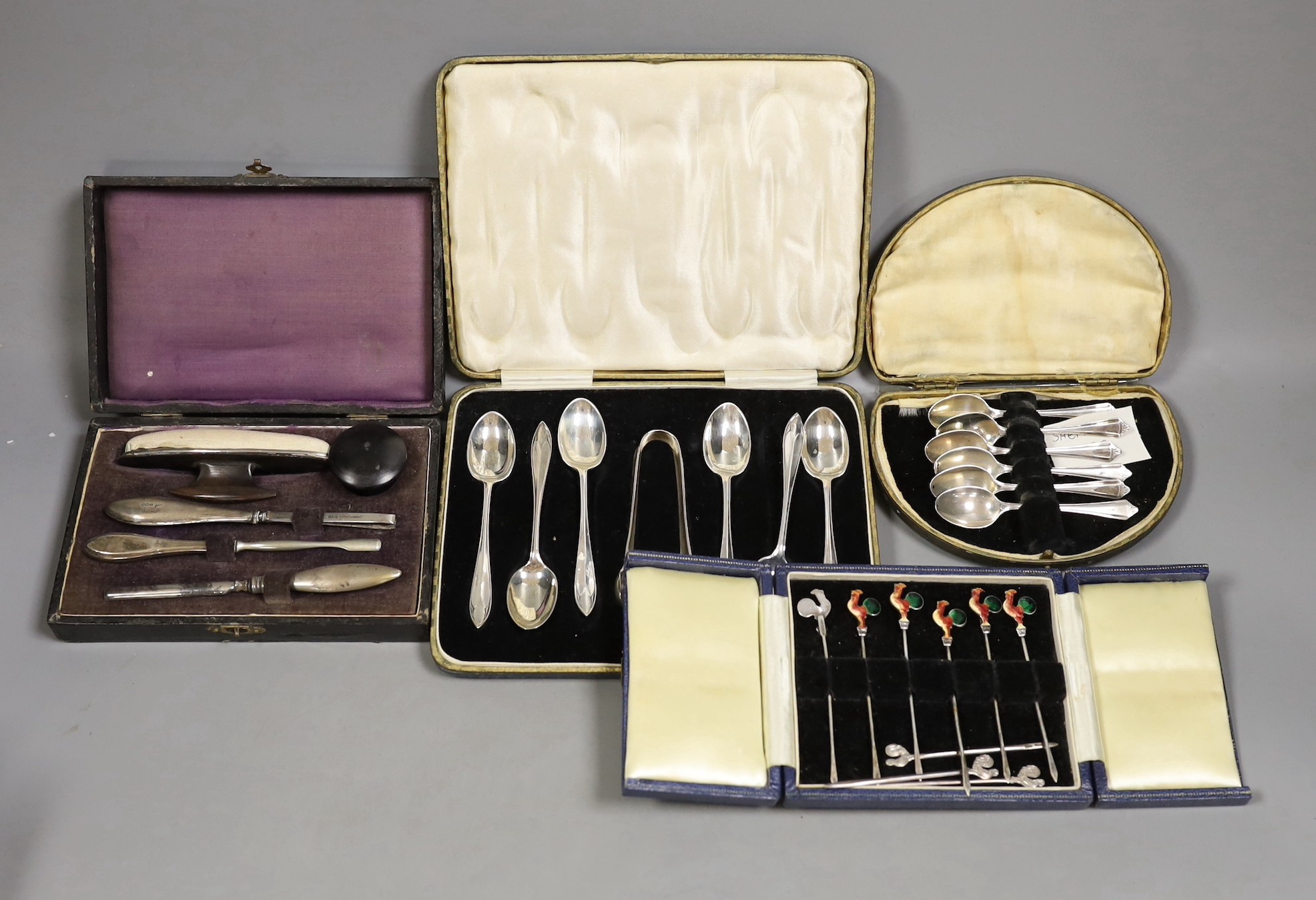 A cased set of six white metal and enamel cocktail sticks and three other cased sets including silver tea and coffee spoons and a manicure set.